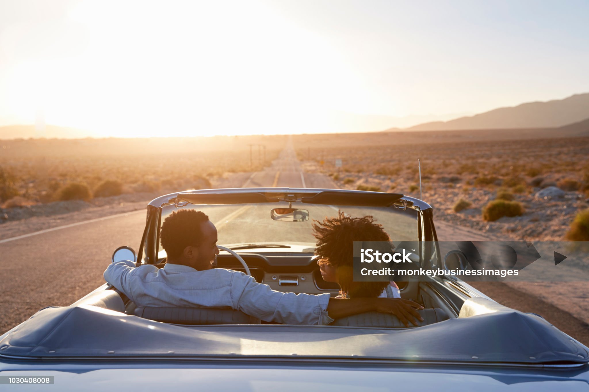 rear-view-of-couple-on-road-trip-driving-classic-convertible-car-towards-sunset-stockpack-istock